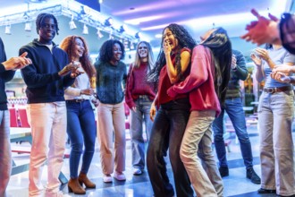 Group of young multiethnic friends enjoying a weekend together dancing and having fun in a bowling
