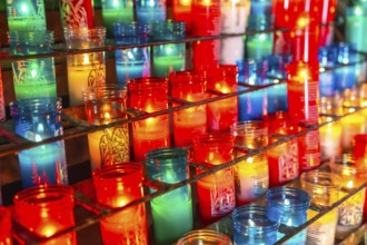 Colorful votive candles burning on a metal rack inside the montserrat monastery, creating a warm