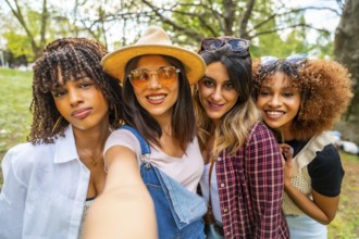 Four cheerful young women smiling and taking a selfie in a park, enjoying their time together in