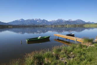 Jetty with green and black boats on a quiet lake in front of a mountain panorama, Hopfen am See,