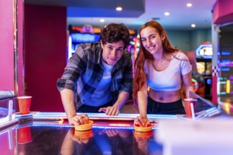 Multiethnic friends having fun together playing air hockey in a colorful amusement arcade