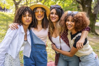 Four diverse young women are hugging, enjoying a carefree day together in a park, embodying unity