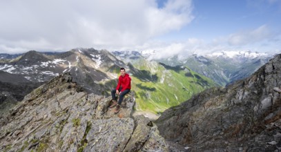 Mountaineer sitting on a rock, on a steep rocky ridge, on the summit of the Lasörling, view of the