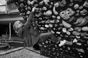 Elderly woman, 65 years old, climbing on climbing wall, urban, concrete, black and white,
