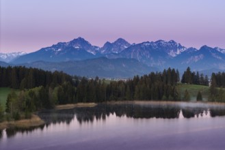 Alpine panorama with a calm lake and mountains in the background in front of sunrise,