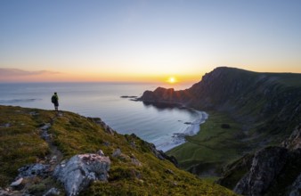 Mountaineer in front of view of coastal landscape at sunset, cliffs and summit of Måtind or