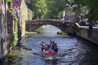 Tourist boat sailing under a historic bridge on a canal, canals, Bruges, West Flanders, Belgium,
