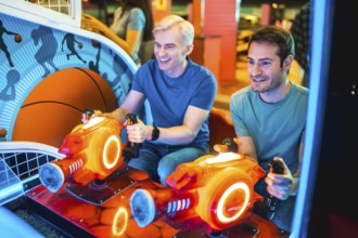 Two young men enjoying a friendly competition on an arcade game machine, illuminated by colorful