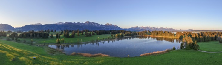 Panoramic view of a lake surrounded by forests and mountains at sunset, Hergratsrieder See, Alps,
