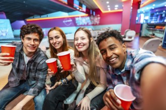 Group of cheerful young multiethnic friends taking a selfie while drinking and having fun in a