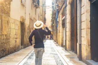Female tourist wearing a straw hat walking down a narrow cobblestone street in the historic city