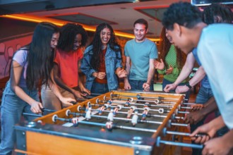 Cheerful multi ethnic friends enjoying a foosball table game in a vibrant entertainment center