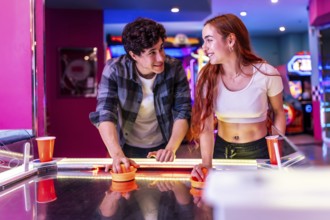 Happy multiethnic friends enjoying a weekend together, playing air hockey in a colorful and dynamic