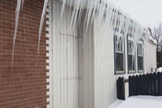 Icicles hanging from snow and ice covered roof of old red brick and white wood plank cladded