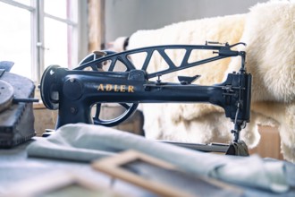 An antique Adler sewing machine in a studio with sewing accessories and leather material, Calw