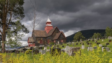 Rapeseed field in front of old church and tree-covered cemetery under a dramatic sky, Dovre church,
