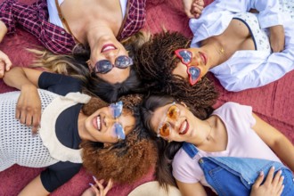 Four diverse young women lying together on a vibrant red blanket, smiling brightly at the camera