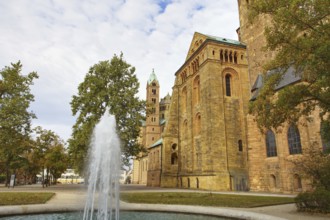 Side view of Speyer Cathedral with towers, trees and a fountain in front of a cloudy sky, Speyer