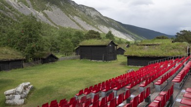 Traditional wooden houses with grass sod roofs, rows of seats with red plastic chairs, ready for an