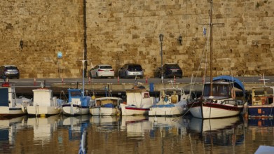 Boats and cars in front of a stone wall, with reflections in the water, harbour area, Rhodes Town,