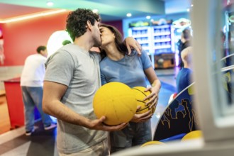 Romantic couple kissing while enjoying basketball and bowling in a vibrant entertainment center,