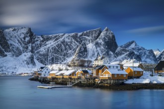 Traditional yellow rorbuer huts on the island of Sakrisøy, snow-capped mountains in the background,
