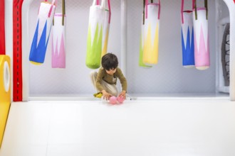 Preschooler playing with pink plastic balls in a colorful soft play area with small punching bags