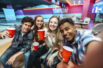 Group of cheerful young multiethnic friends taking a selfie while enjoying drinks and bowling at
