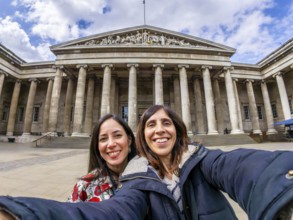 Two happy female tourists are taking a selfie with a fisheye lens in front of the british museum in