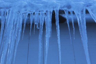 Long icicles and thick heavy ice hanging from roof edge of grey wood plank cladded building in