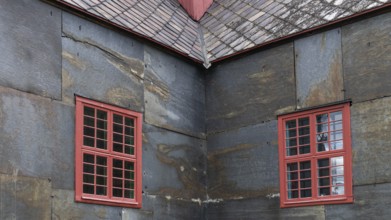 Detailed view of a corner of a building with red window frames on slate-clad walls, Dovre church,