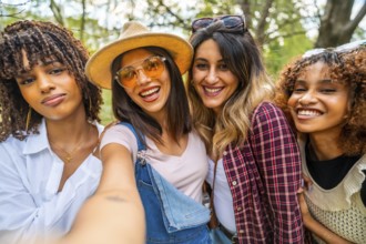 Four cheerful young women embracing and taking a selfie in a park, enjoying their time together