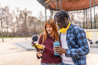 Two young content creators are recording a video in a park, using a smartphone with a microphone