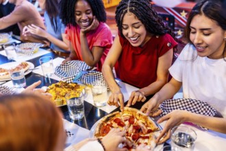 Cheerful multi ethnic friends enjoying pizza and nachos at a bowling alley restaurant, celebrating