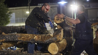 ©Udo Rein, A man cuts wood with a chainsaw while the other helps, Easter fire Psinthos, Holy