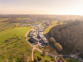 Industrial area next to a town, surrounded by green landscape and a forest at sunset, Gechingen,
