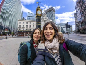 Two happy tourists taking a selfie with a fisheye lens in front of a historic clock tower in