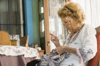 Senior woman enjoying retirement while sewing vibrant fabric, sitting comfortably beside a table