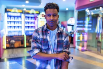 Young man standing in a vibrant arcade, surrounded by colorful lights and gaming machines, enjoying