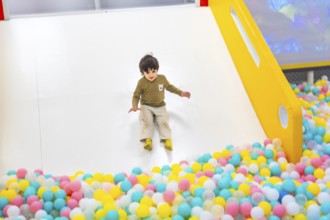 Young boy joyfully sliding into a vibrant, colorful ball pit at an indoor playground, surrounded by