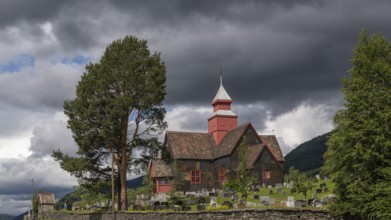 Historic church with cemetery under dark clouds and a tree in the foreground, Dovre, Fylke