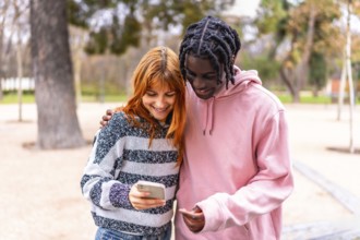 Happy multi ethnic couple sharing social media content on a smartphone while walking in a park