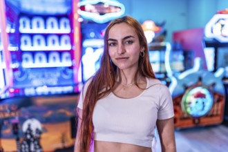 Stylish young woman standing in a vibrant amusement arcade, surrounded by colorful neon lights and