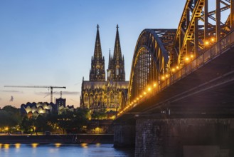 Cologne Cathedral, illuminated in the evening. Hohenzollern Bridge, railway bridge over the Rhine.