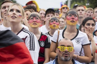 Women wearing make-up in the German national colours watch the football match in the fan zone at