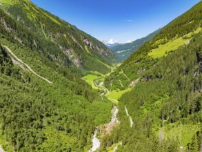 A sunlit valley with green meadows and densely wooded mountains under a clear sky, Stilluptal,