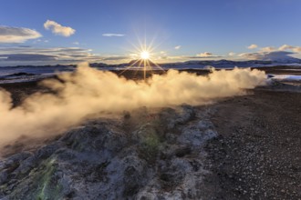 Hot springs and geothermal area in front of mountain landscape in winter, sunbeams, cloudy mood,
