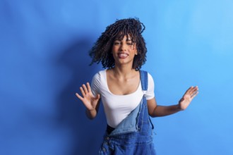 Young woman with curly hair dancing joyfully against a vibrant blue backdrop, embodying carefree