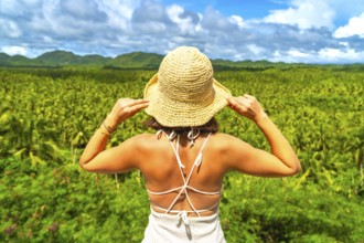 Young woman enjoying the view of a wide coconut plantation in siargao island, philippines, holding