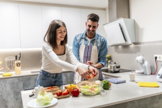 Cheerful couple smiling and preparing a healthy salad together in a modern kitchen, enjoying their